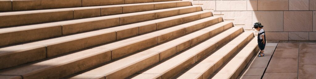 Man on mountain|Construction|Man working at computer|Man stood on mountain pondering the enormity of devops|Construction of DevOps|Small child at bottom of steps
